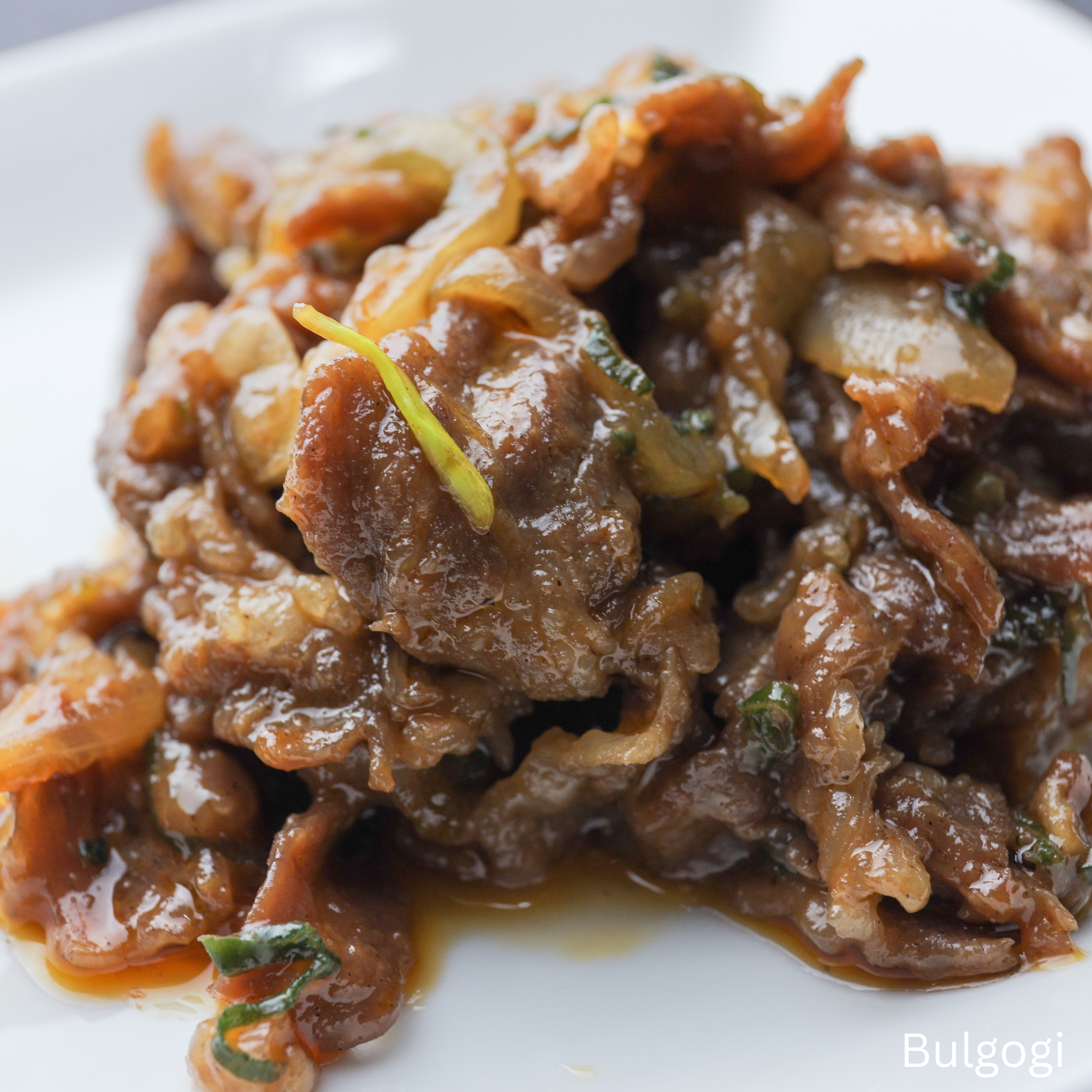 Close-up of Korean Bulgogi, marinated beef stir-fried with onions and scallions, served on a white plate.