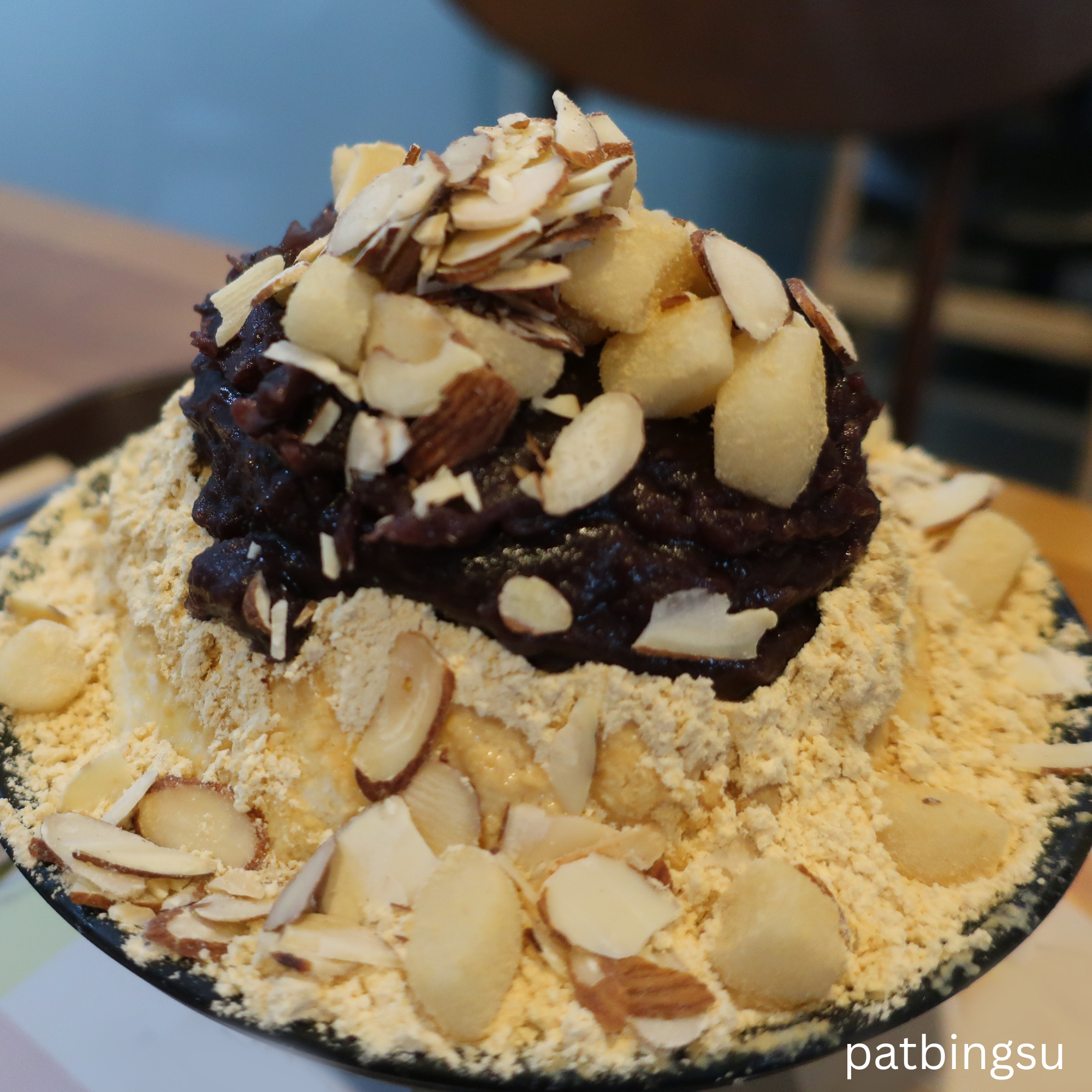 Korean Patbingsu dessert with shaved ice, sweet red bean paste, mochi rice cakes, roasted almond slices, and soybean powder topping.